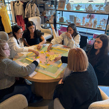 Group of women playing Mahjong game in a store setting with shelves and products in the background.